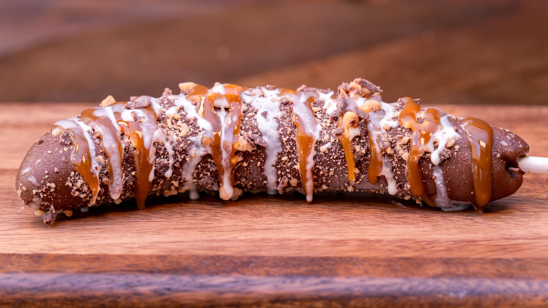 Frozen Banoffee Banana: Milk chocolate-dipped frozen banana with toffee pieces, caramel sauce, and white chocolate drizzle (New)